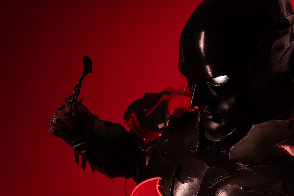 Close-up of a dark-themed superhero cosplay with a striking red backdrop.