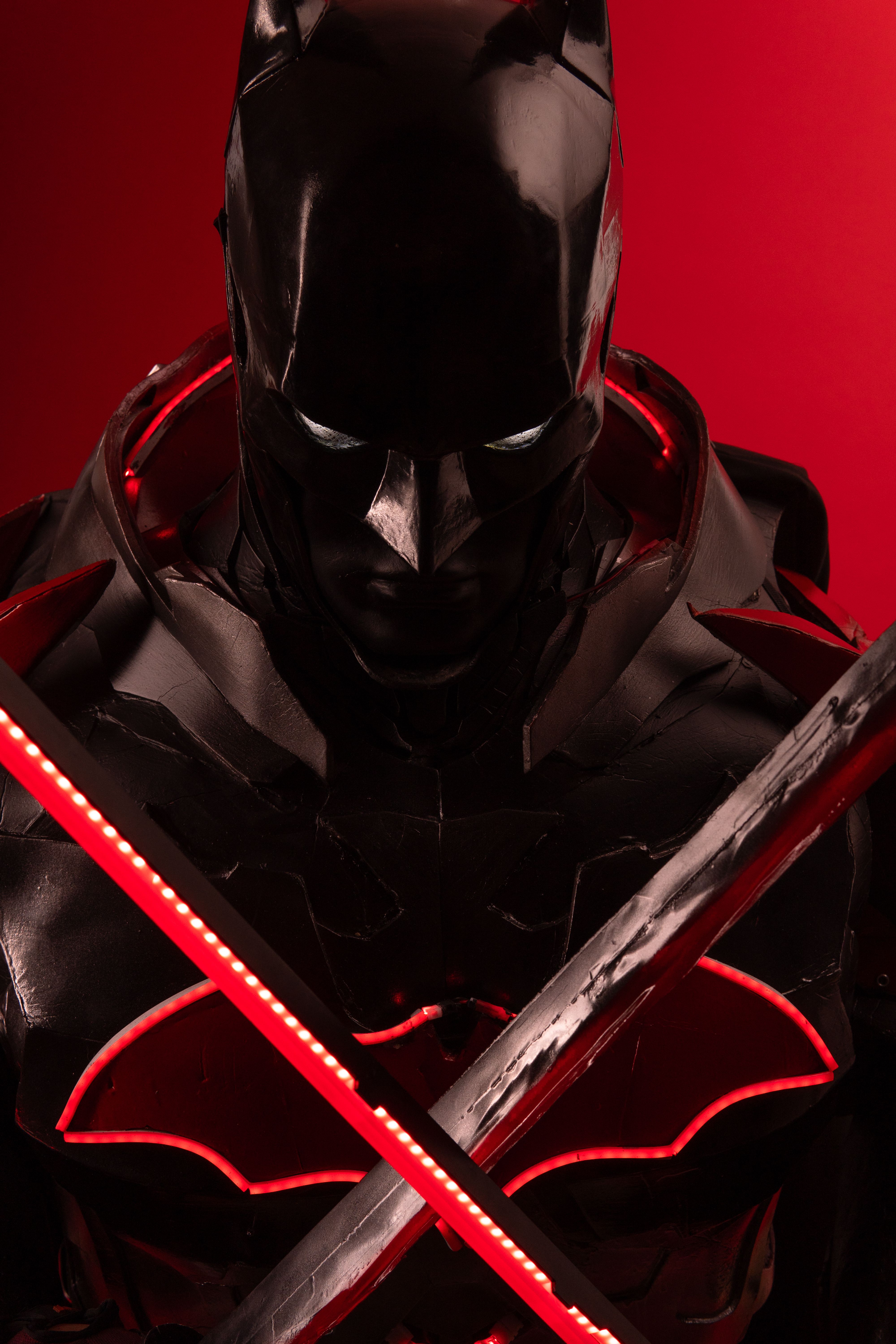 Close-up of a detailed Batman cosplay with red accents and swords, set against a bold red background.