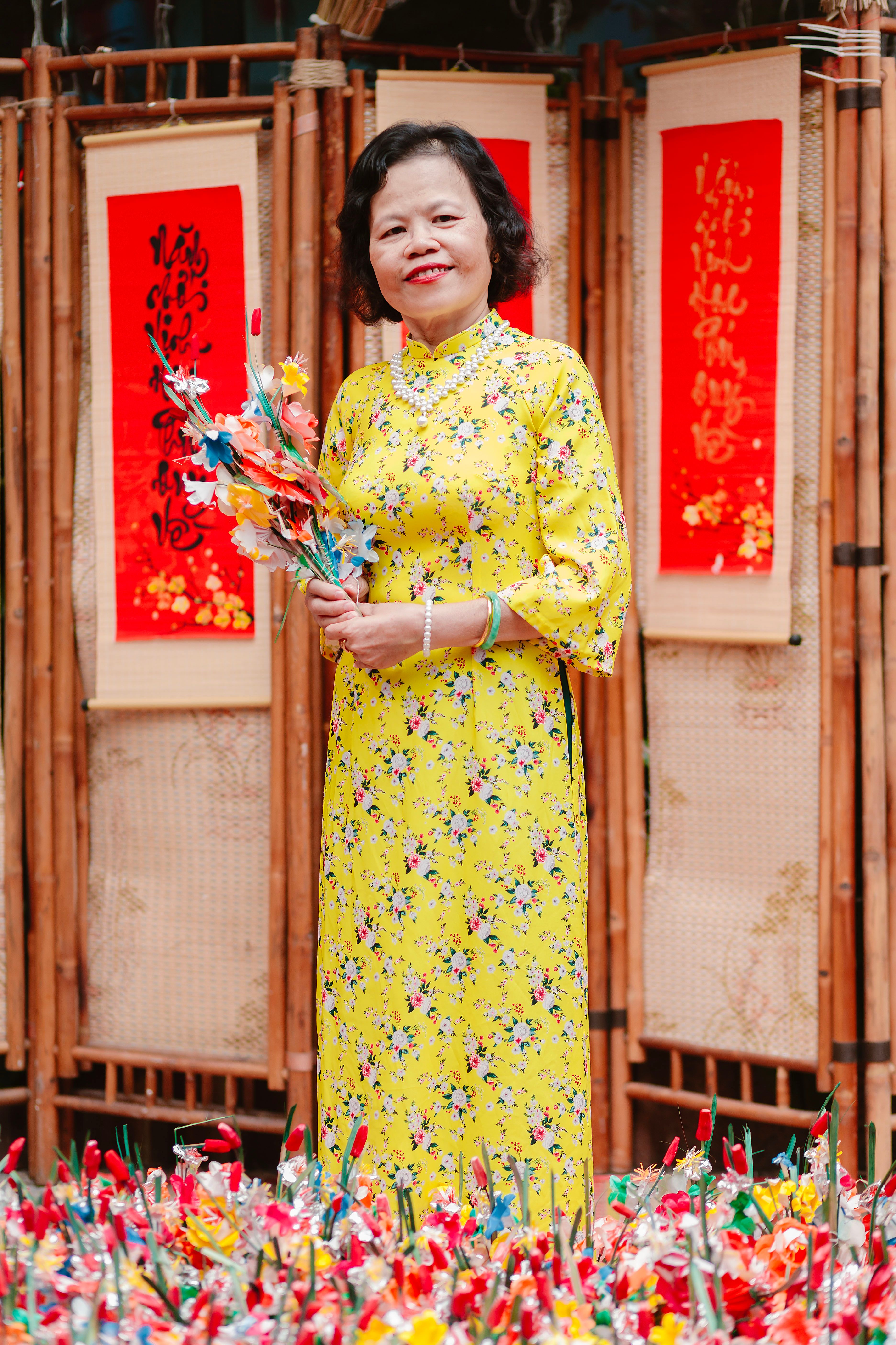 Woman in vibrant yellow ao dai holding floral bouquet amidst festive decorations.