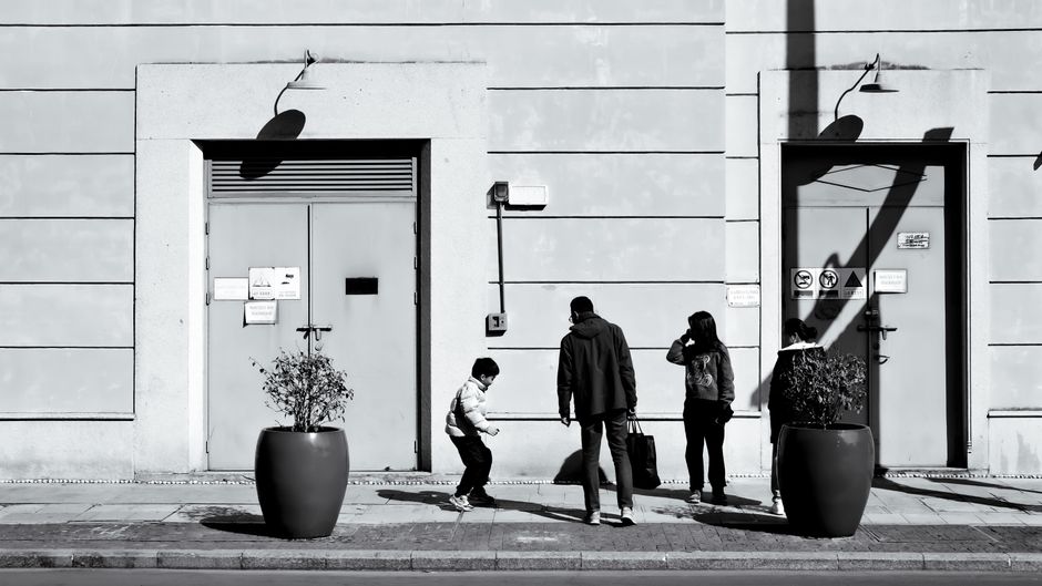 Una fotografía en blanco y negro de una familia caminando por una calle de la ciudad, proyectando sombras.