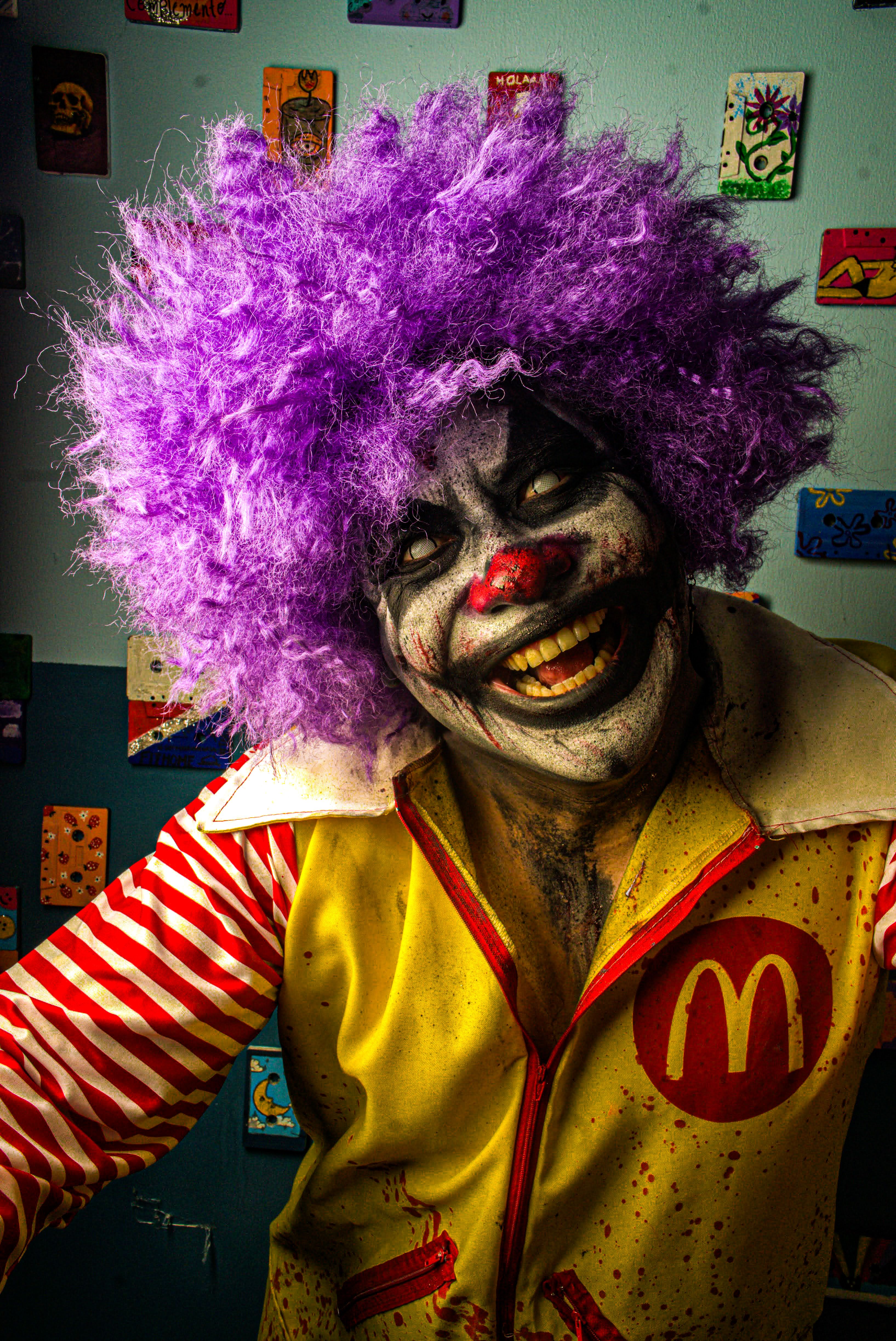 Vibrant clown with purple wig and colorful costume posing indoors.