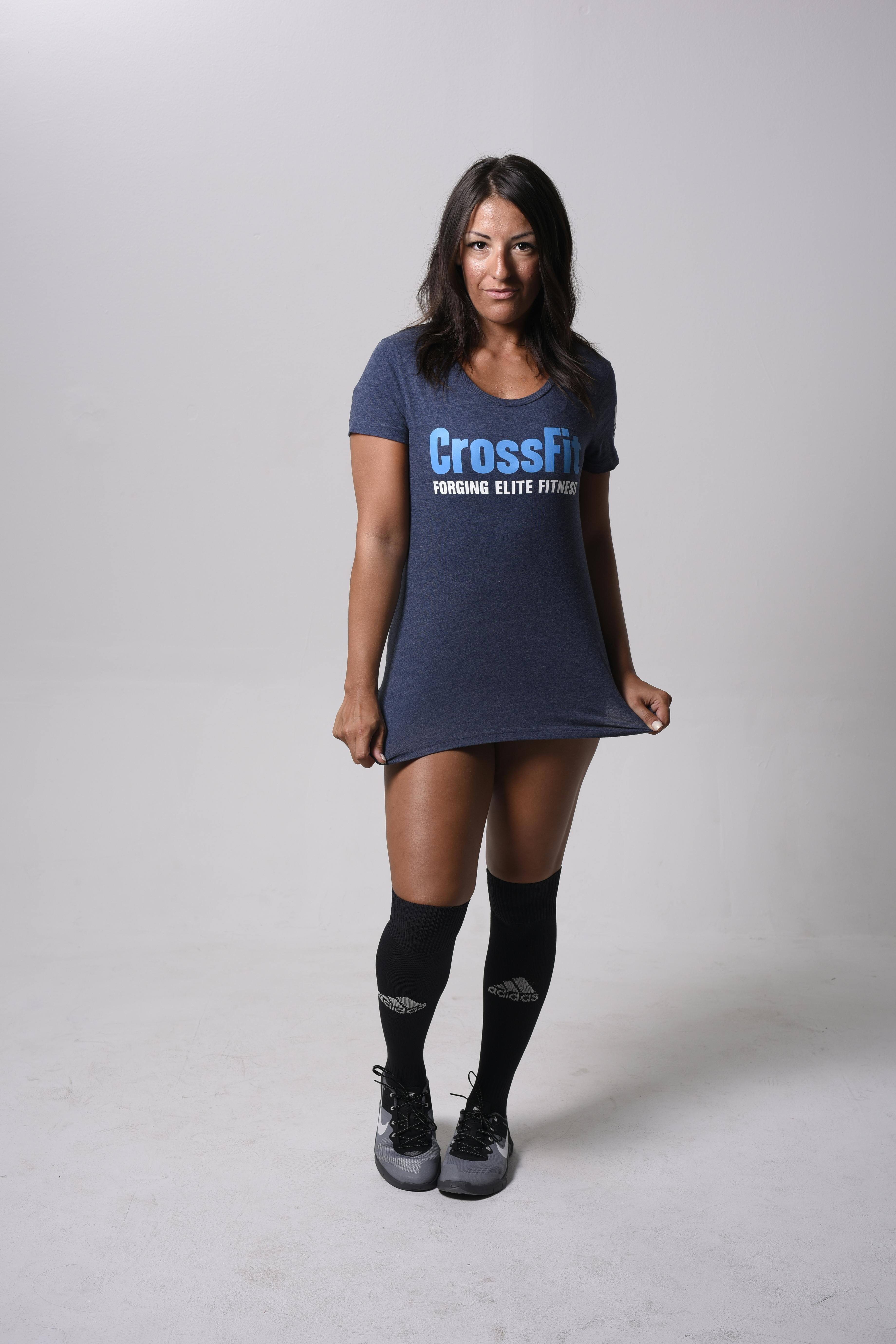 Smiling woman wearing CrossFit t-shirt and socks in a bright studio setting.
