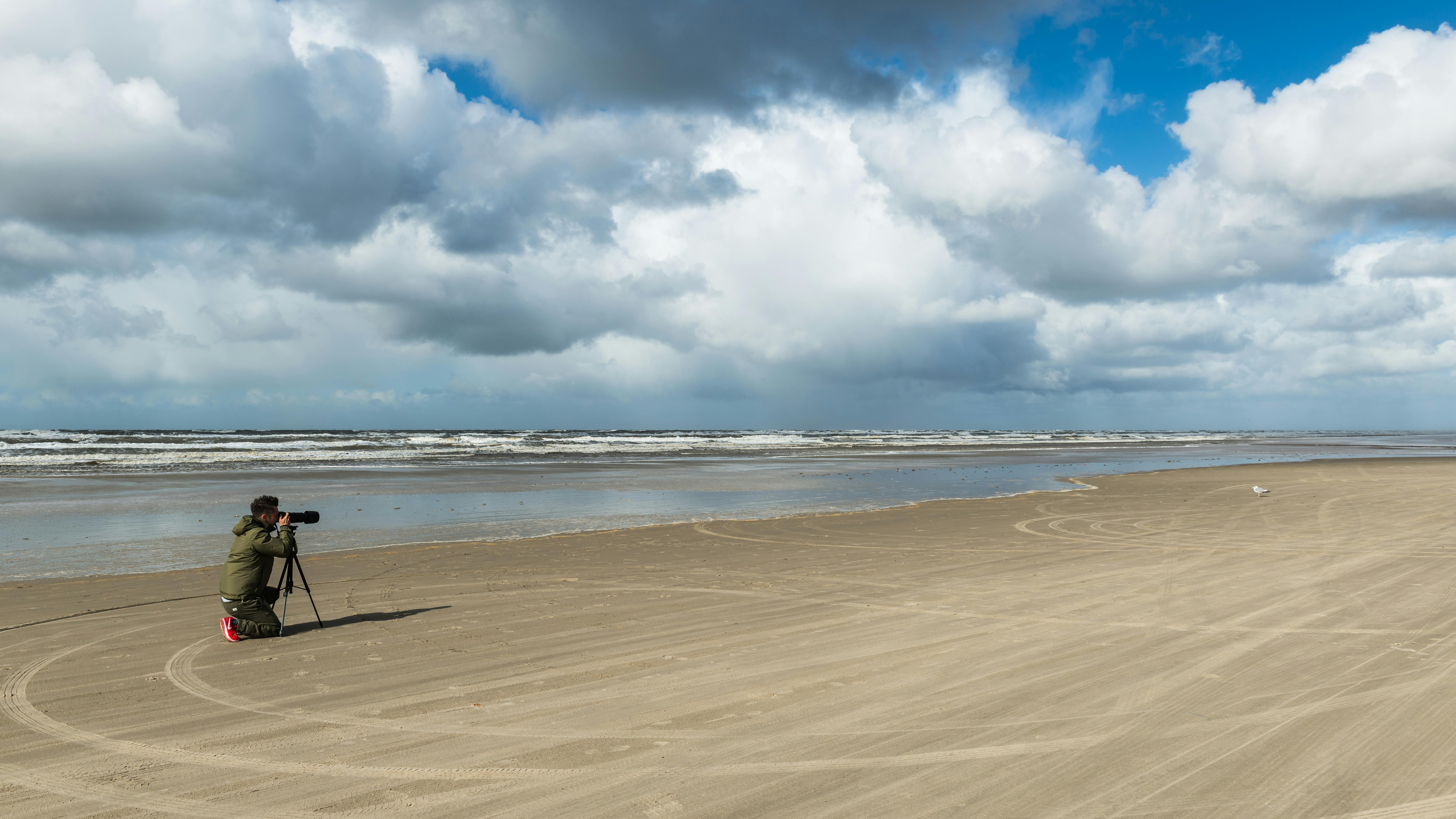 Photographer on Henne Kirkeby's tranquil beach capturing serene coastal views under dramatic clouds.
