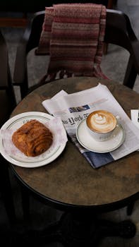 Warm café scene with coffee, pastry, and newspaper on a rustic table.