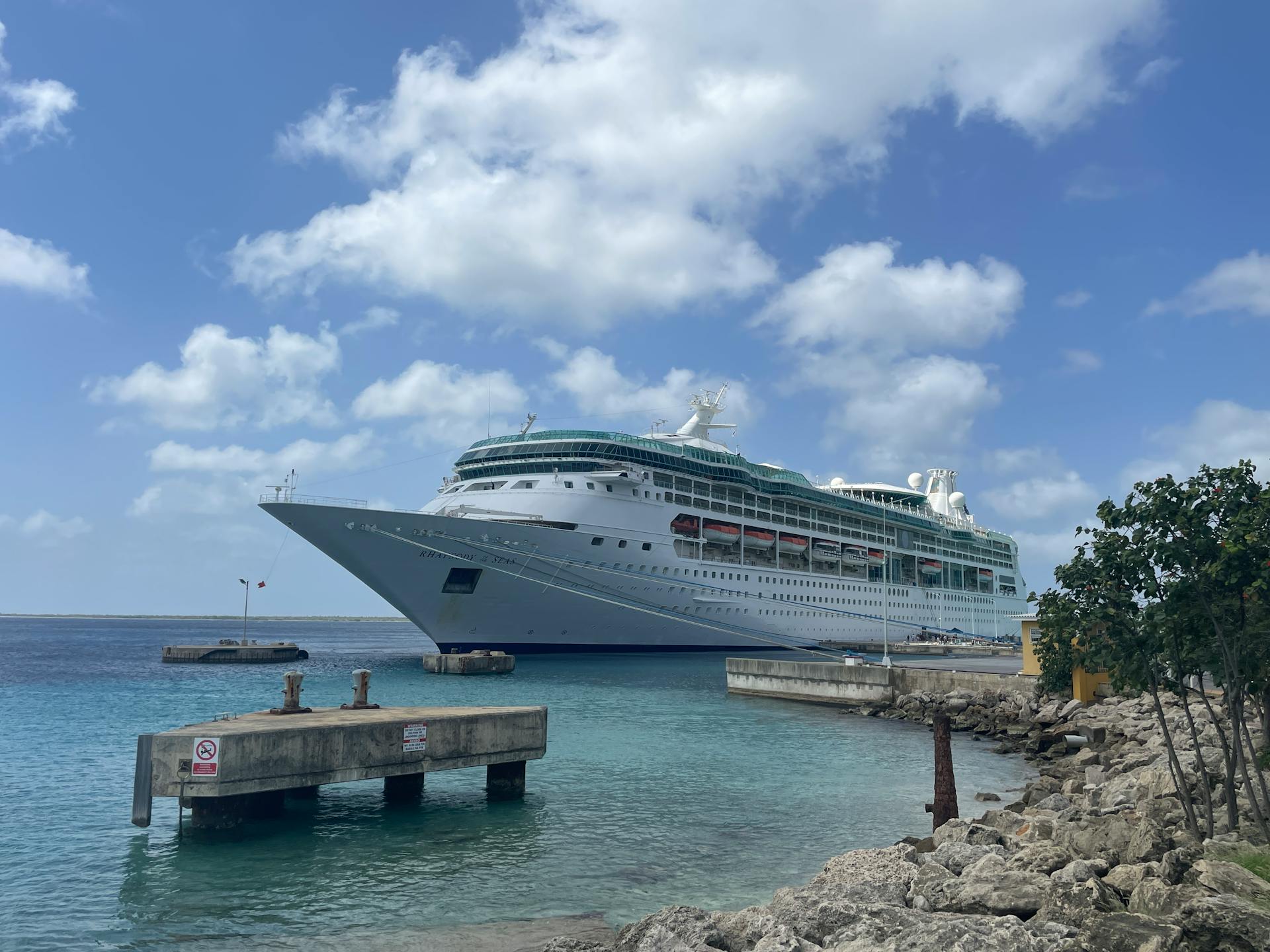 A luxurious cruise ship docked in a crystal clear tropical harbor, under a bright blue sky.