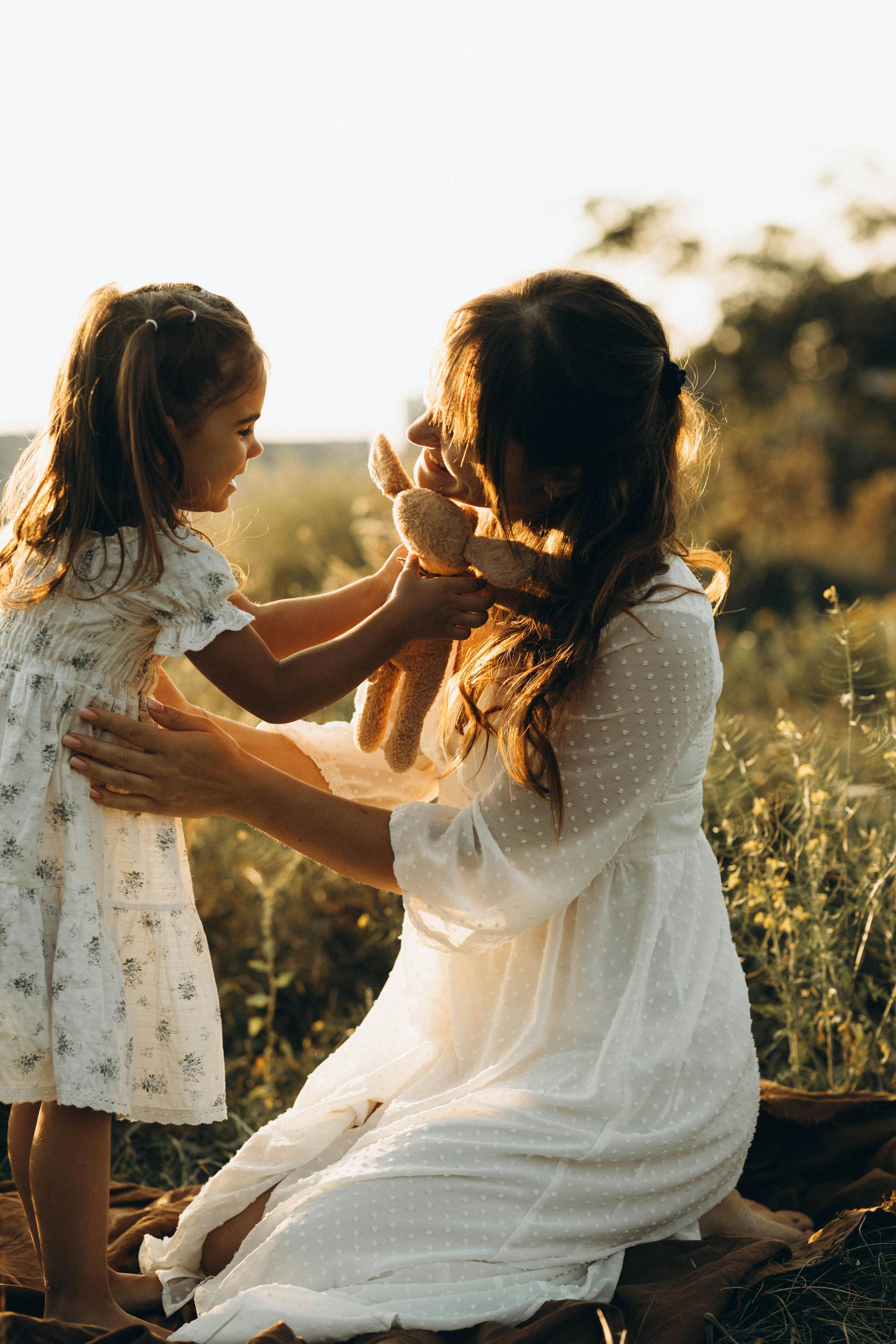 A mother and daughter share a joyful moment in a sunny outdoor field, fostering love and connection.