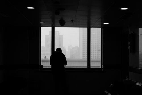 Free Silhouette of a person looking out a window at a modern cityscape in black and white. Stock Photo
