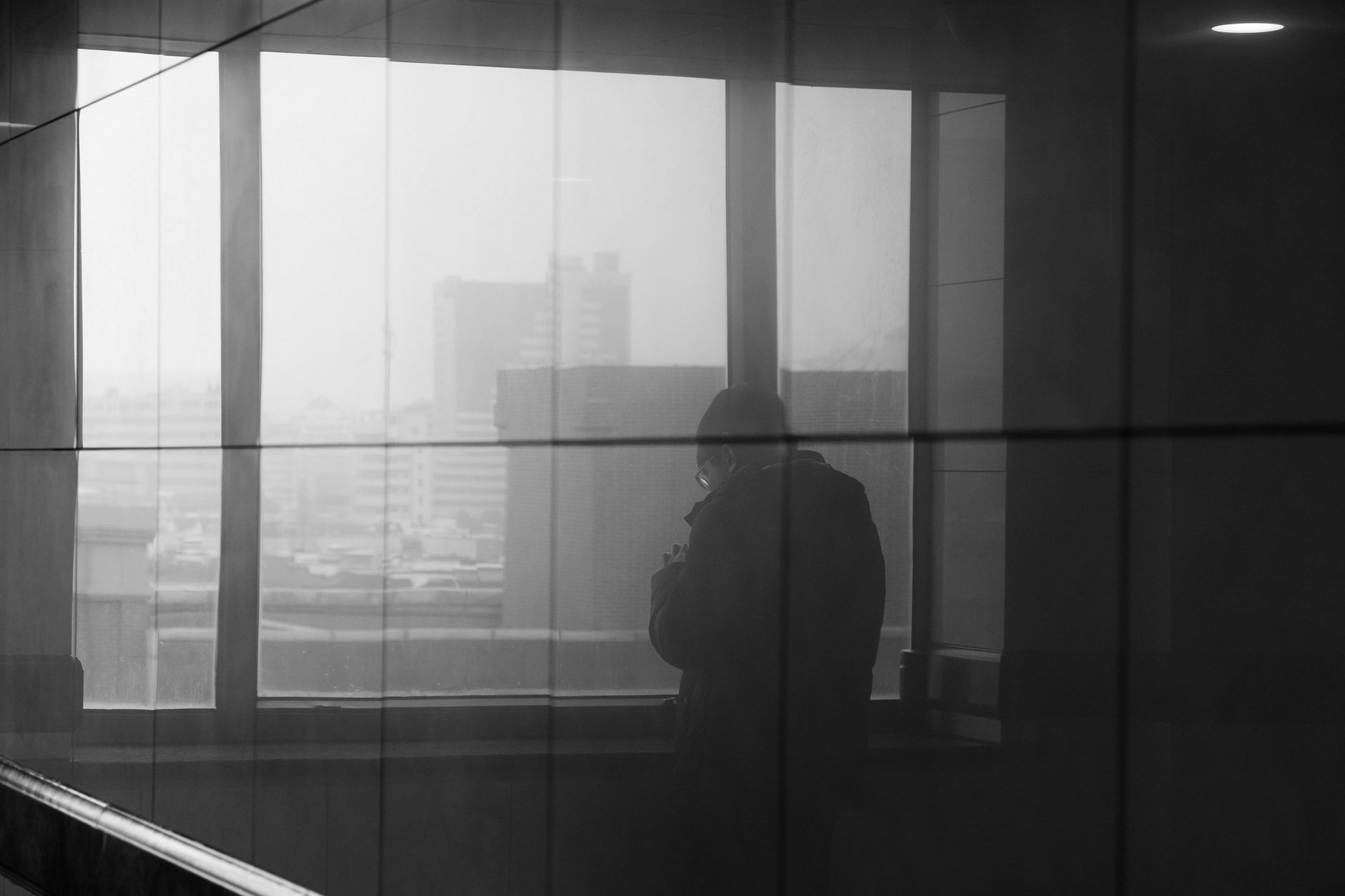 Silhouette of a person reflecting in a window, overlooking a city in black and white.
