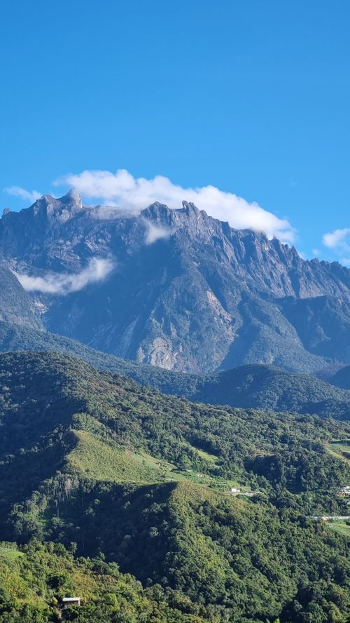 Free Mount Kinabalu towering under a clear blue sky with green foothills in Sabah, Malaysia. Stock Photo