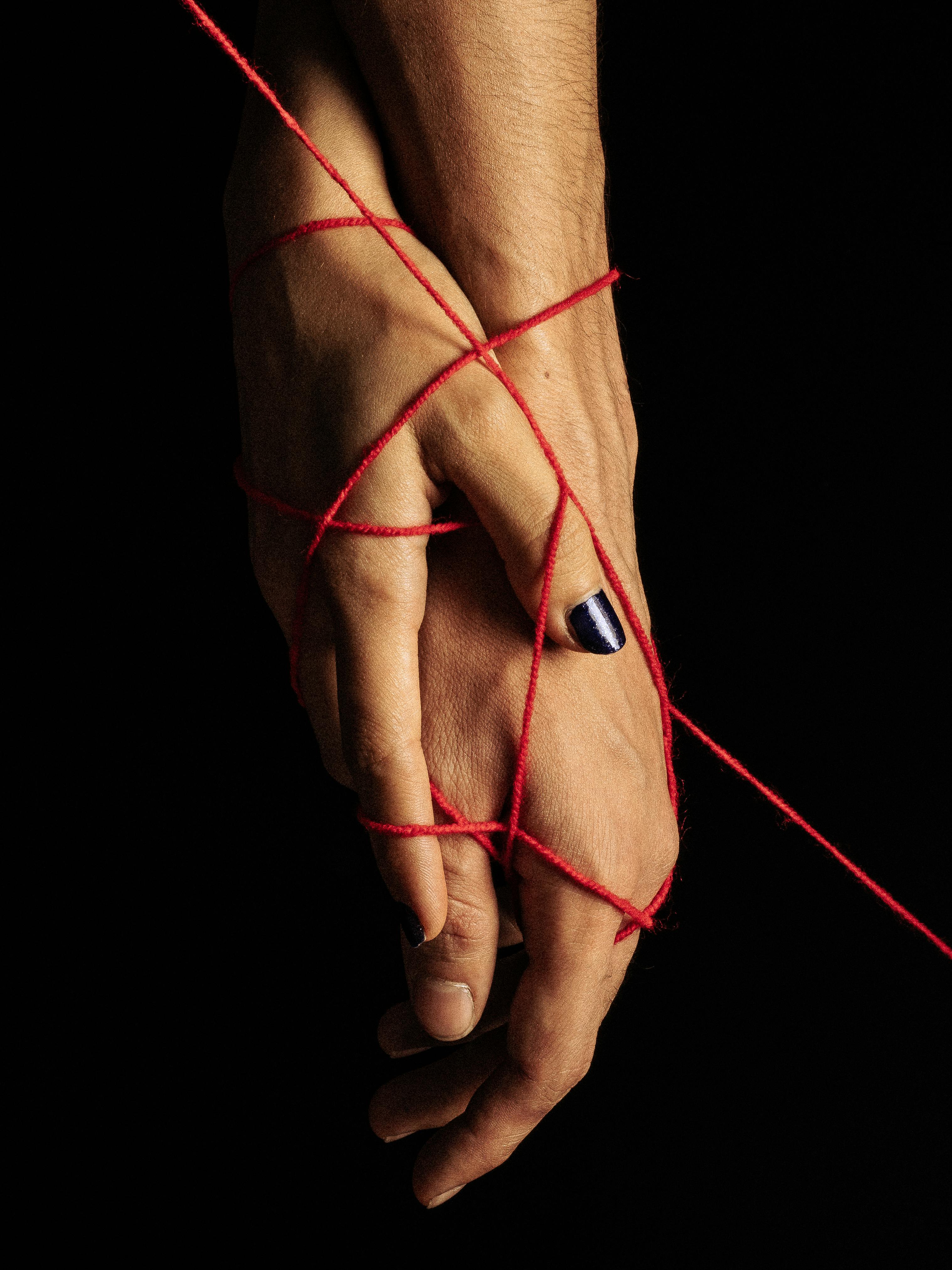Artistic portrayal of hands entwined with red thread symbolizing connection and unity