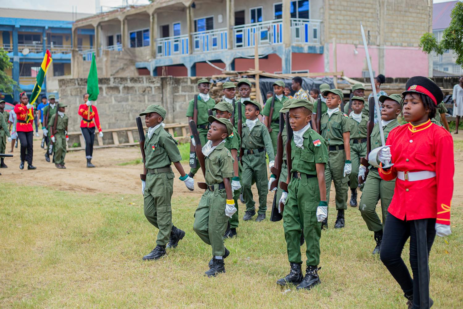 Ghanaian cadet group practicing military drills in school setting.