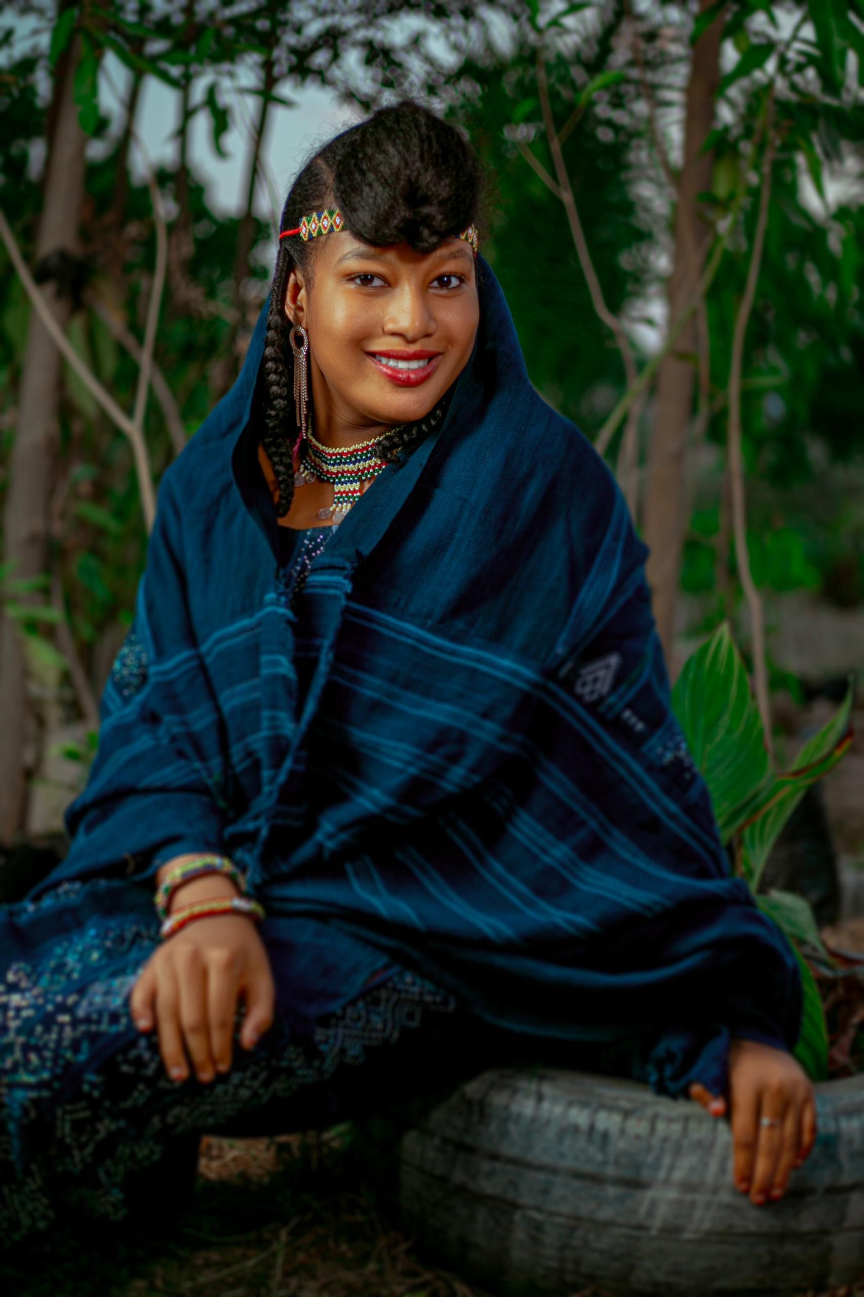 A woman in colorful Nigerian traditional attire smiling in nature.