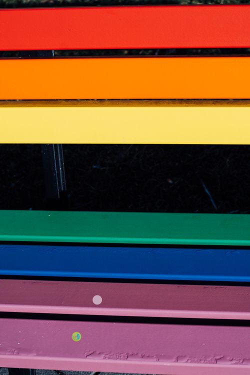 Free Colorful painted park bench with rainbow stripes in a public garden setting. Stock Photo