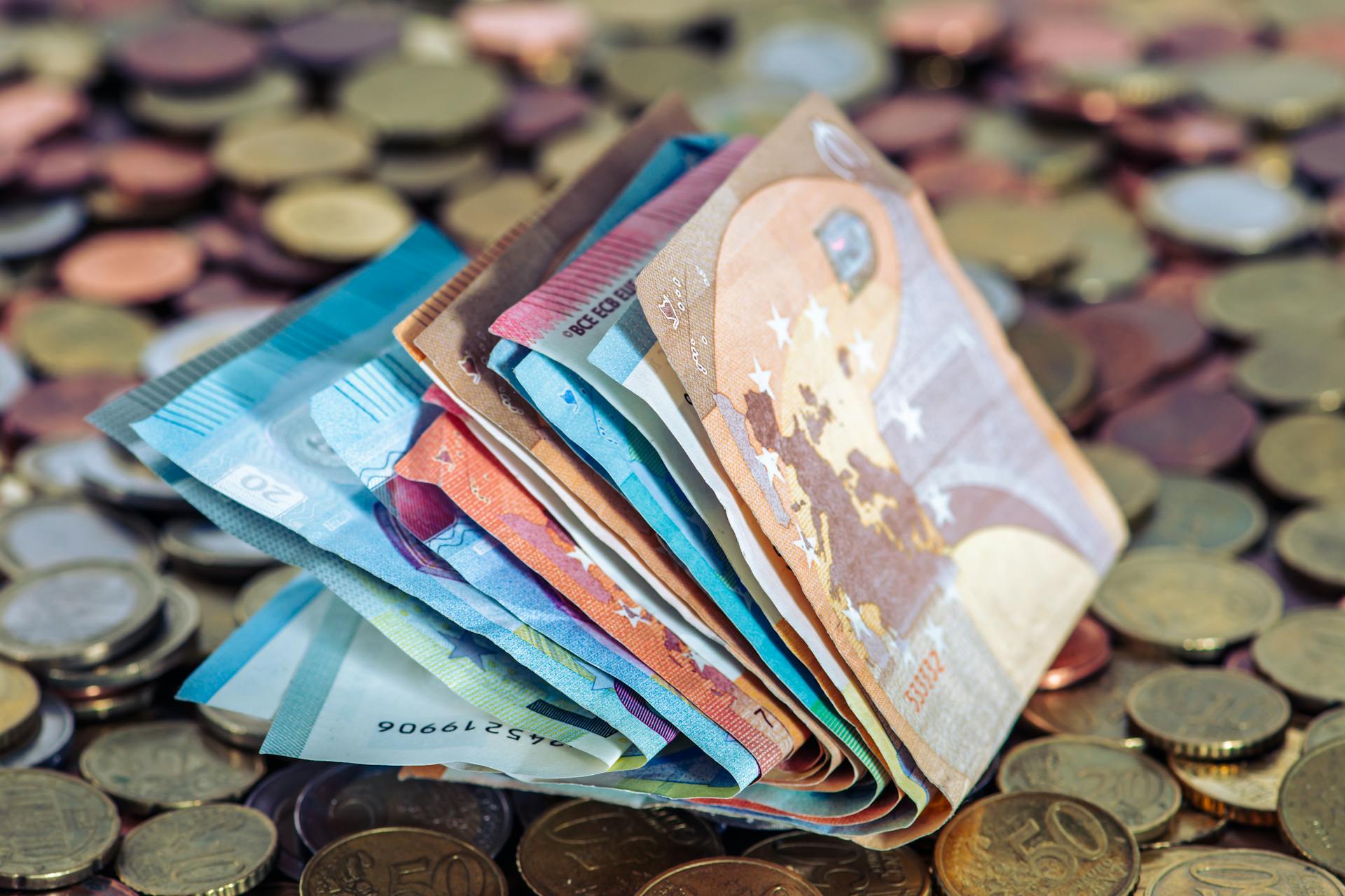 A stack of euro banknotes and scattered coins symbolize wealth and finance.