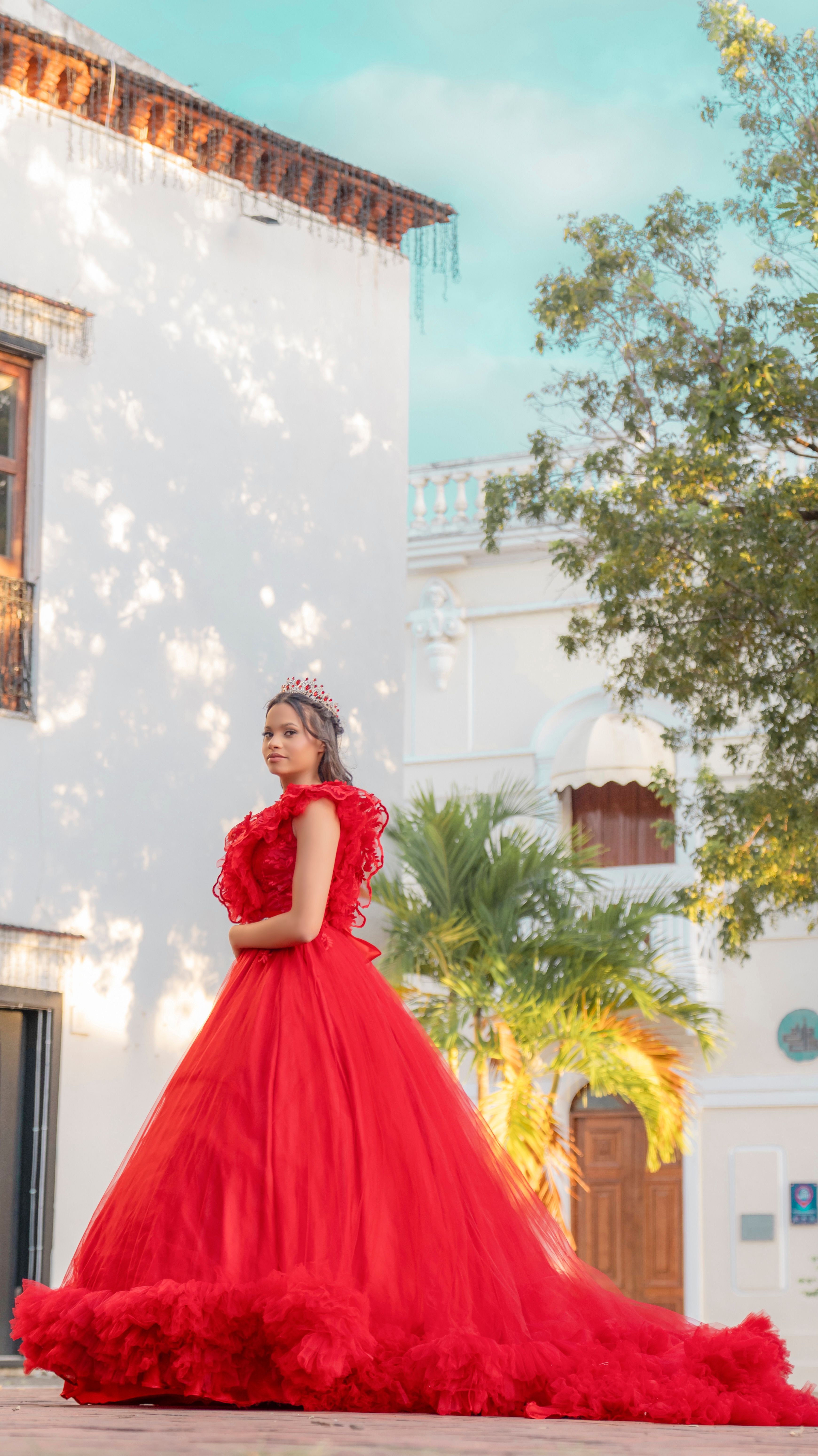 A teenager wearing a stunning red dress poses gracefully outdoors in Santo Domingo, Dominican Republic.