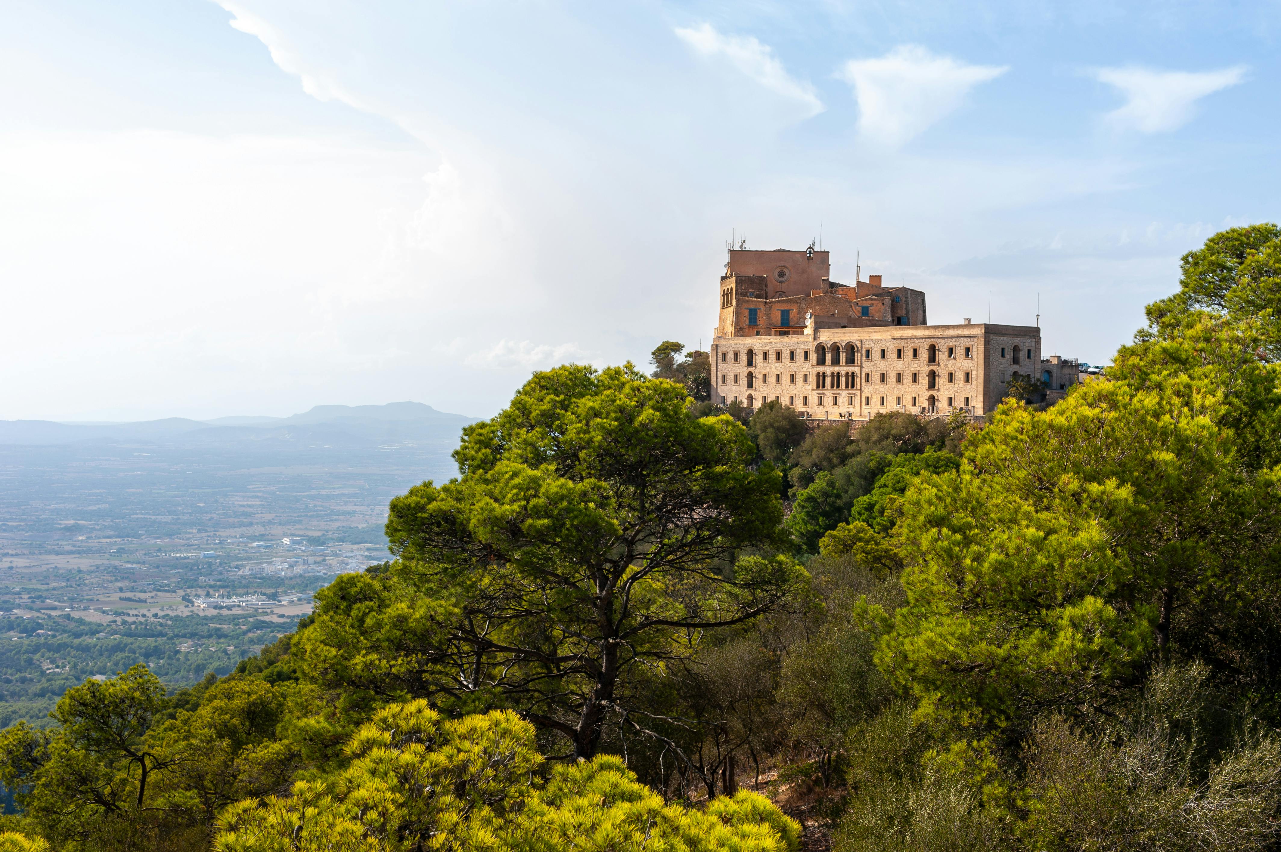 Gratis Vista panoramica di uno storico monastero sulla cima di una collina di Maiorca, circondato da una vegetazione lussureggiante e sotto un cielo azzurro. Foto a disposizione