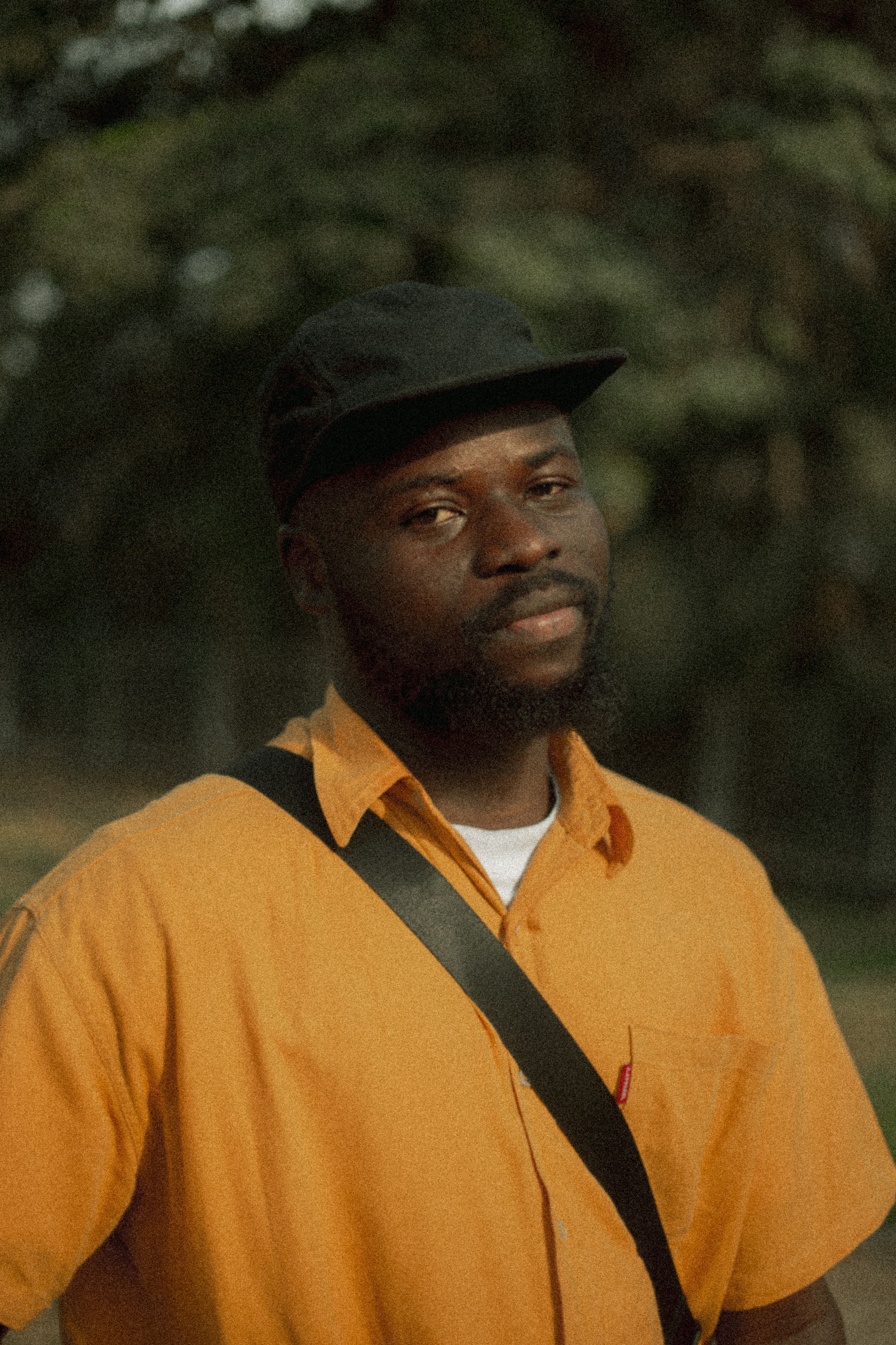 Serene portrait of a man in an orange shirt taken outdoors in Abuja, Nigeria.