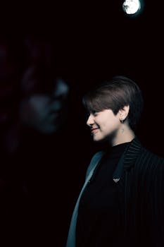 A woman with short hair smiles under spotlight in a dark setting.