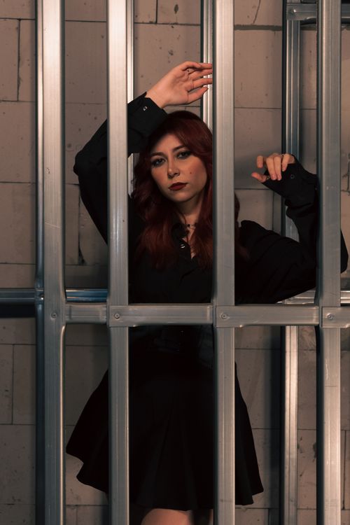 Free Woman in black outfit behind metal bars, conveying a moody, dramatic feel. Stock Photo