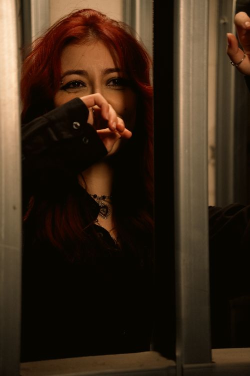Free Dramatic portrait of a woman with red hair looking thoughtful through metal bars. Stock Photo