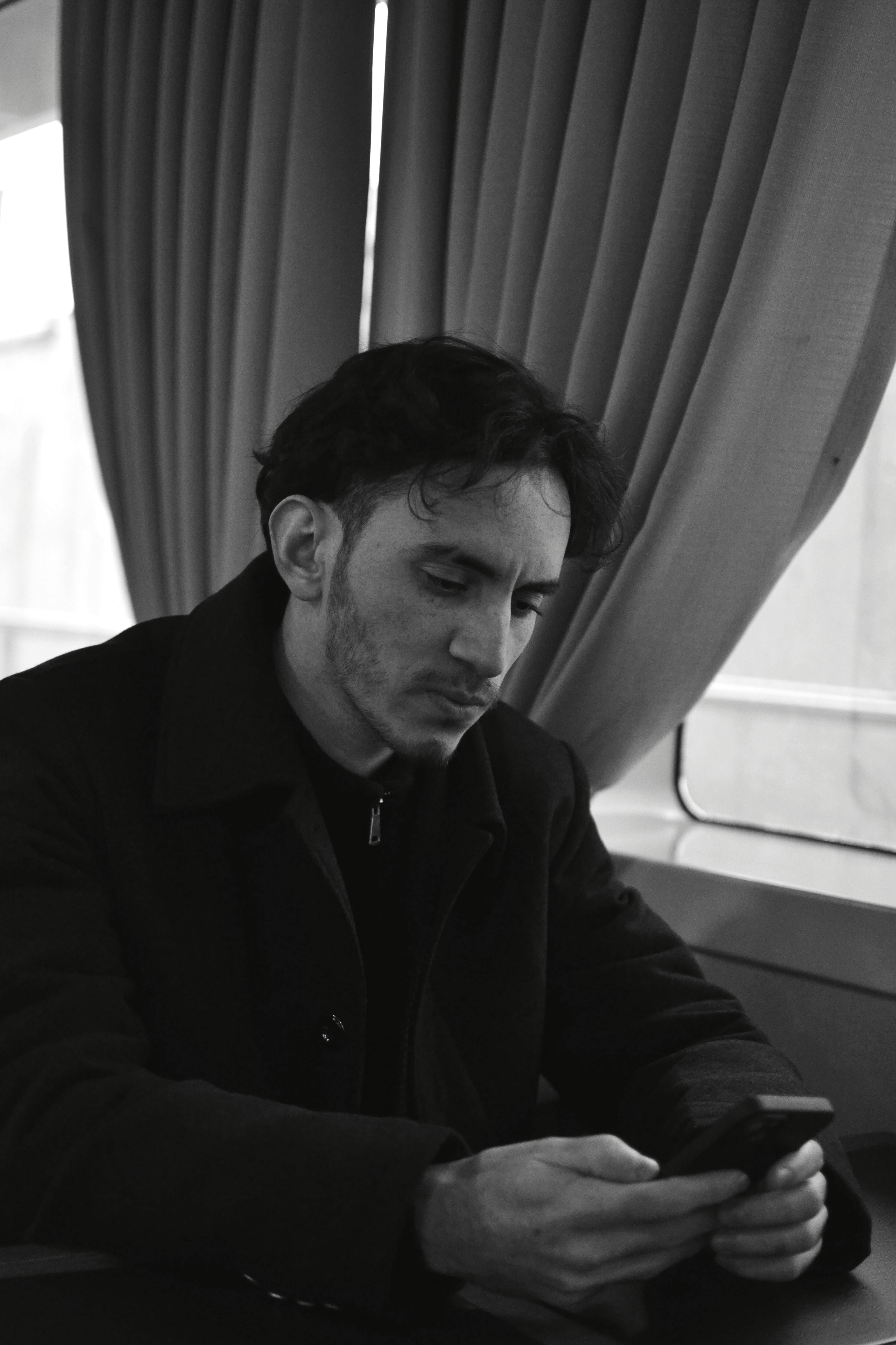 Black and white portrait of a man absorbed in smartphone use, with a contemplative expression.