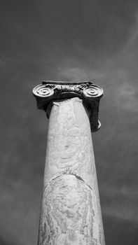 Black and white photo of an ancient Greek marble column in a dramatic sky.