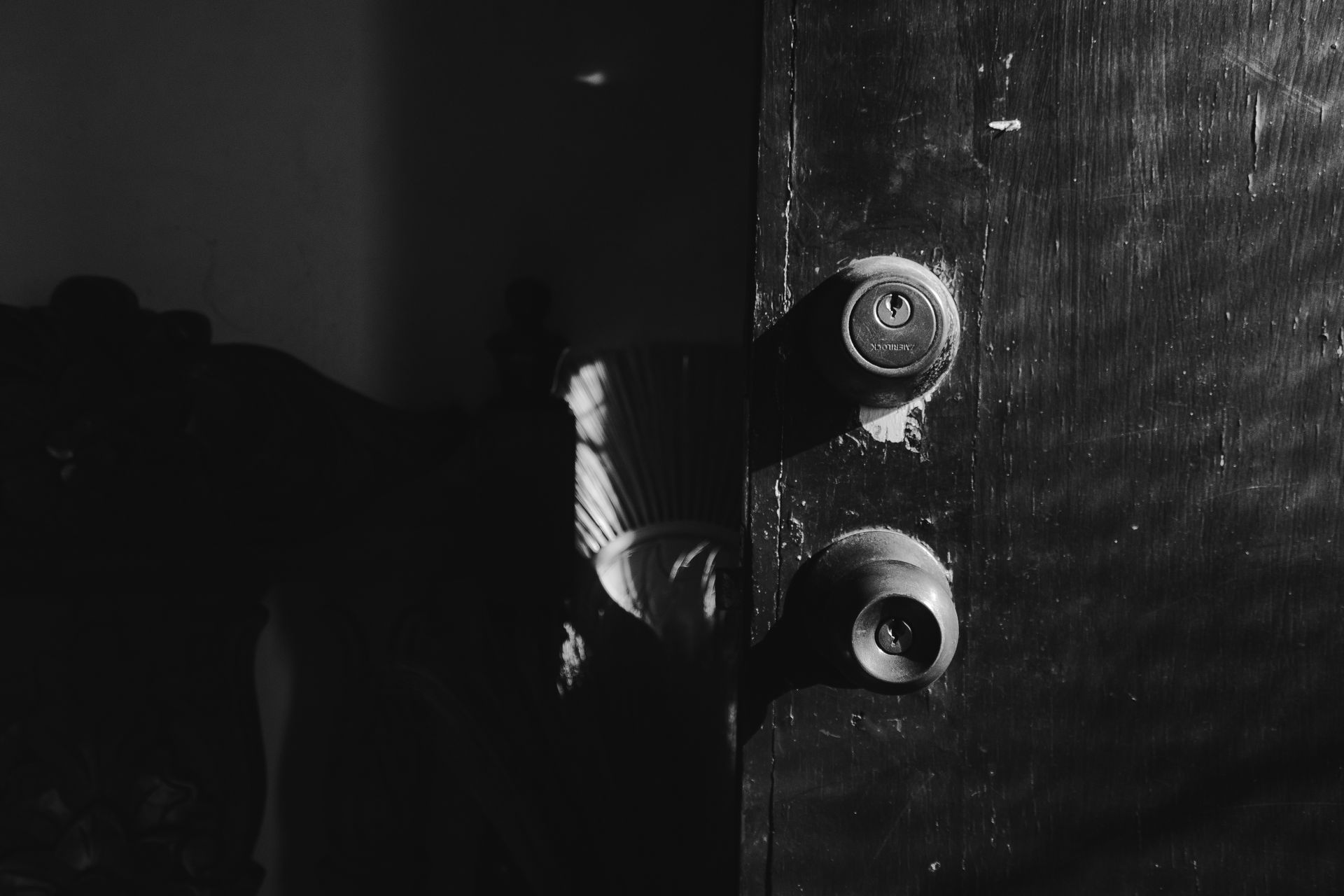 A moody black and white photograph of a door with light and shadows indoors.