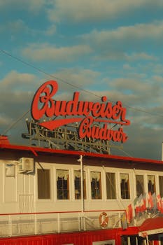Red Budweiser Budvar sign atop a building in Prague, showcasing iconic branding under a blue sky.