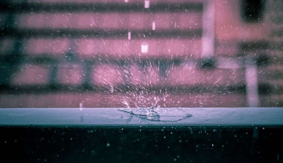 Fotomural Captura dramática de una gota de lluvia salpicando en una superficie con fondo urbano desenfocado.