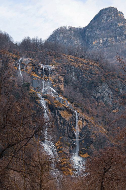 Free Captivating view of a winter waterfall in Chiavenna, surrounded by rugged mountains and leafless trees. Stock Photo