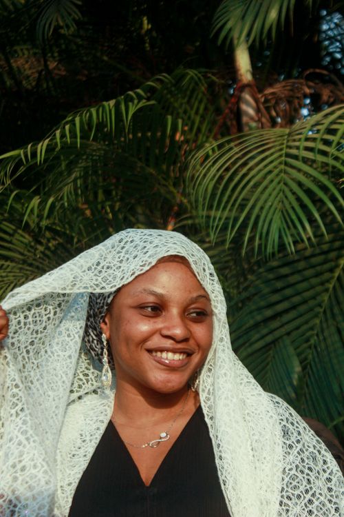 Free A smiling woman with a lace shawl stands in front of lush tropical foliage. Stock Photo