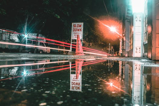 夜晚的城市街道上，水坑反射着路灯的光径