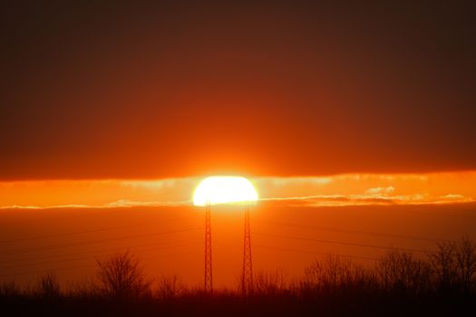 A vibrant sunset silhouetting trees and towers against an orange sky.