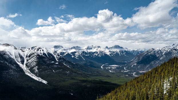 Stunning view of a snow-capped mountain range with lush valley and cloudy sky.