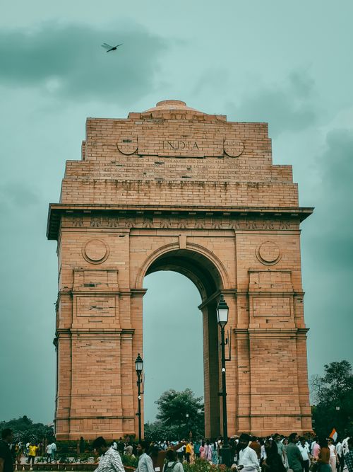 Free A view of the iconic India Gate in New Delhi with a crowd gathered underneath and a cloudy sky. Stock Photo