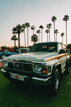 A classic SUV parked amidst palm trees at sunset during a car show in Dubai.