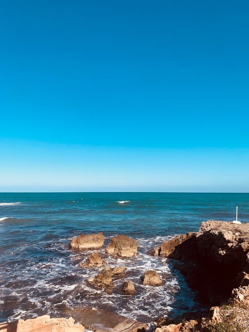 Free Serene ocean view over rocky coastline under clear blue sky. Stock Photo