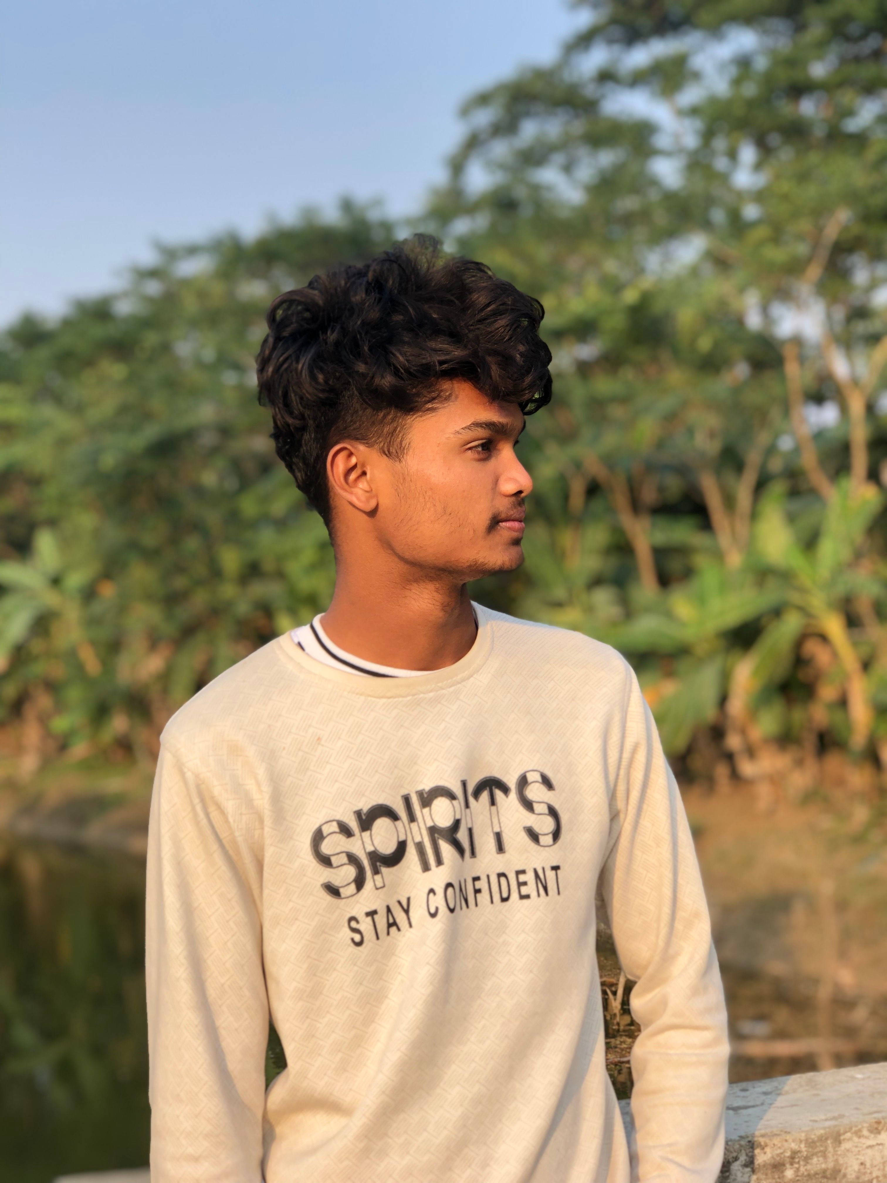 Young man in a casual setting near a pond with lush greenery in Karachi, Pakistan.