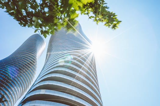 在晴朗的蓝天下，现代摩天大楼在阳光中闪耀，树枝繁茂