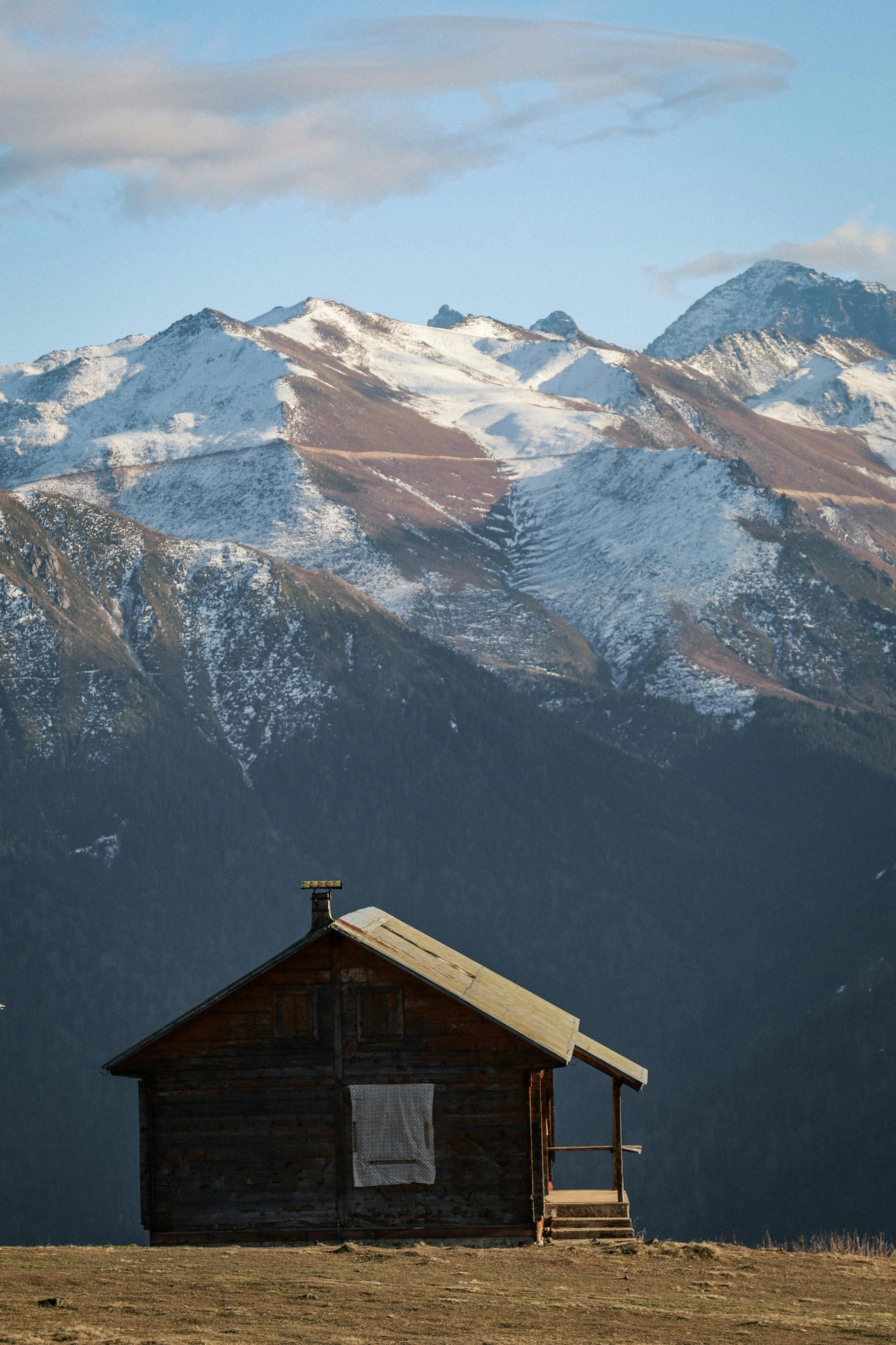 A wooden cabin sits peacefully on a snowy plateau with majestic mountainous backdrop in Rize.