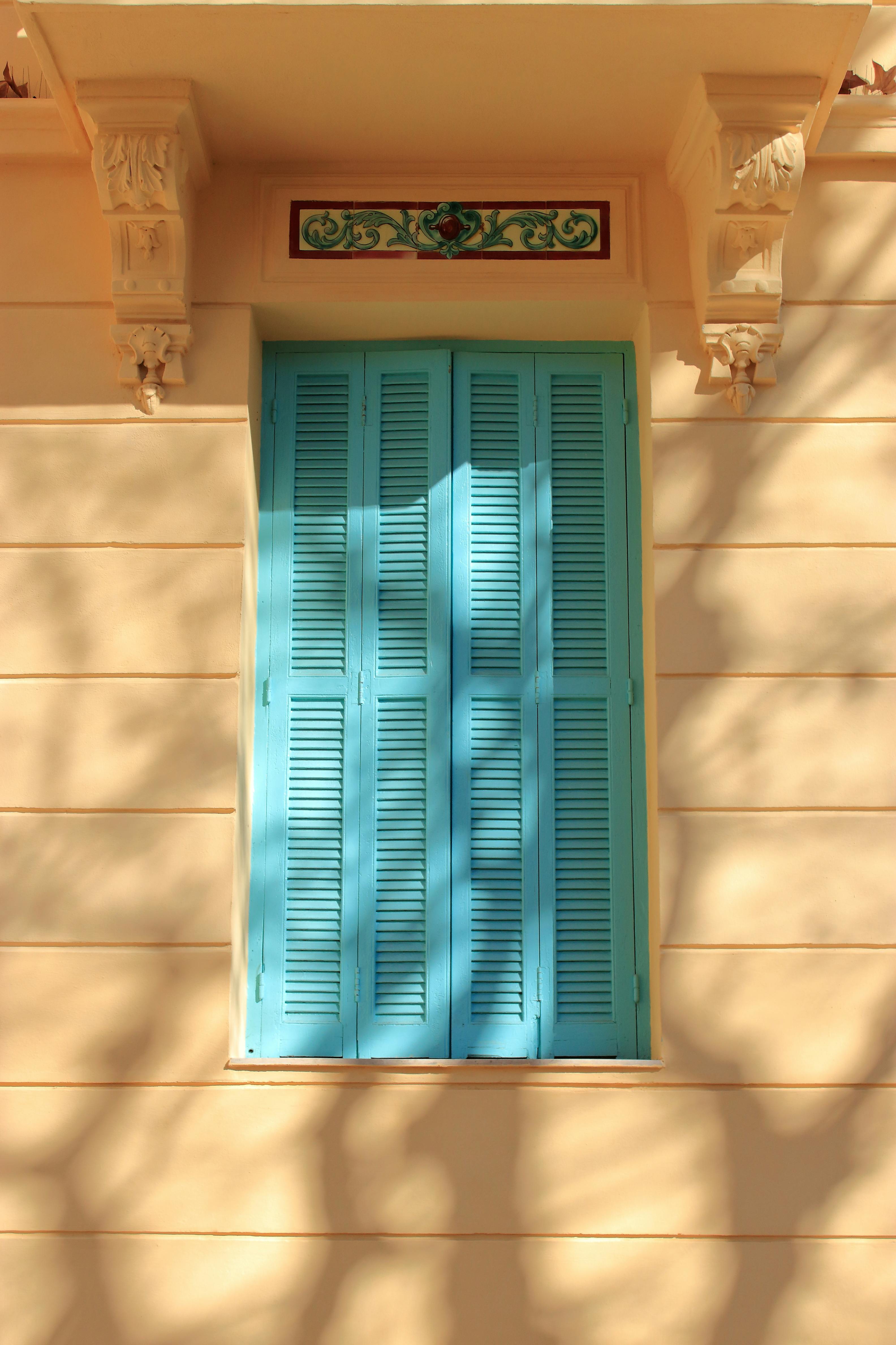 Artistic image of blue window shutters on a beige wall with artistic shadow patterns.