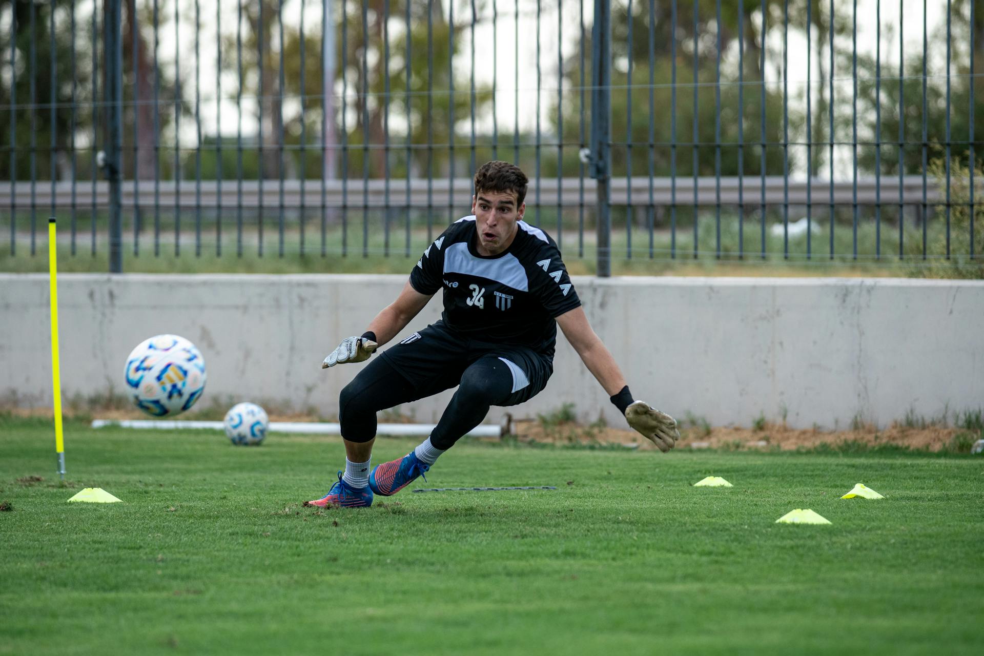 A young male goalkeeper practicing on a grass field outdoors, focusing on agility and training skills.