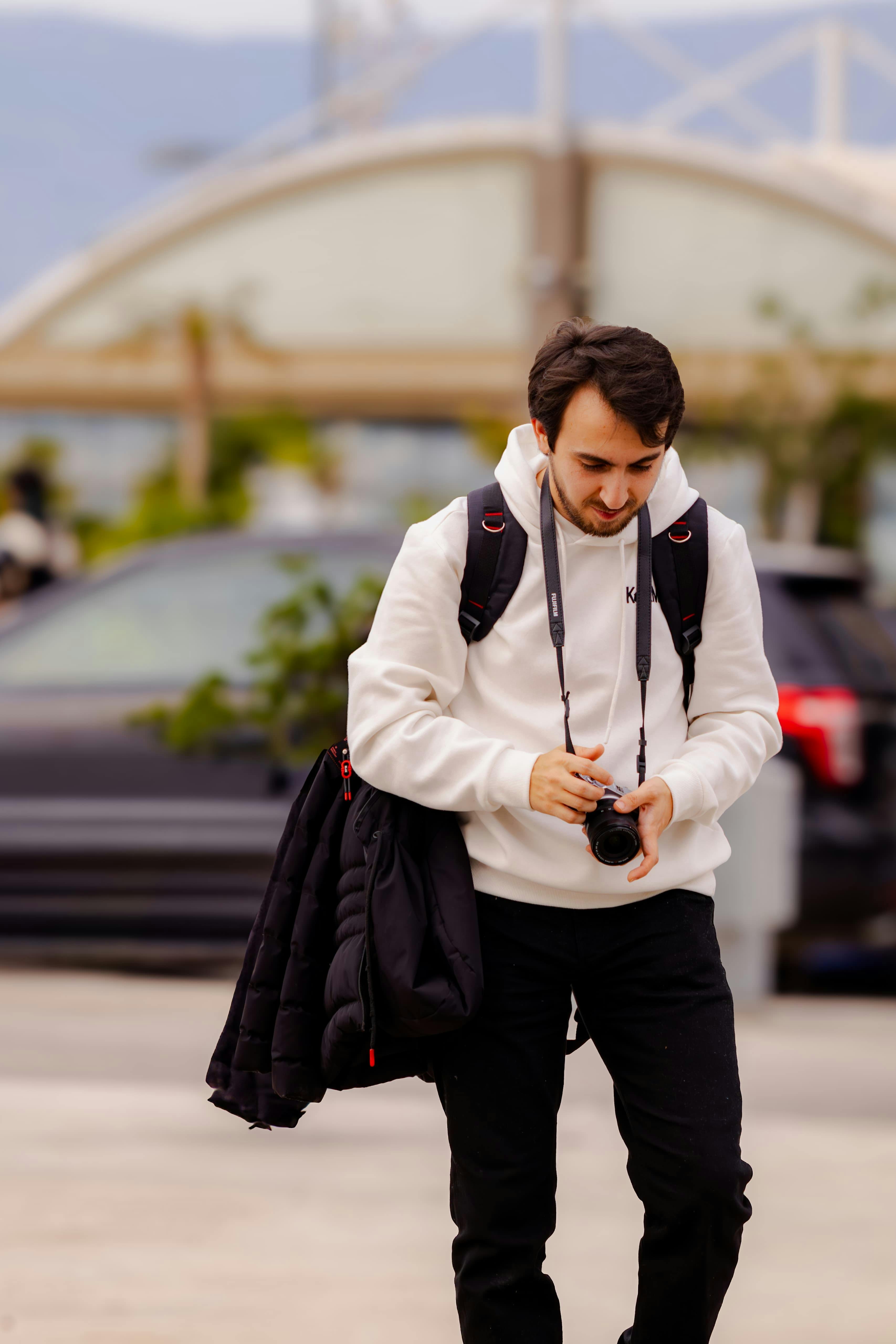 Gratis Maschio adulto con macchina fotografica e zaino, vestito casualmente all'aperto. Catturato in un momento spontaneo. Foto a disposizione