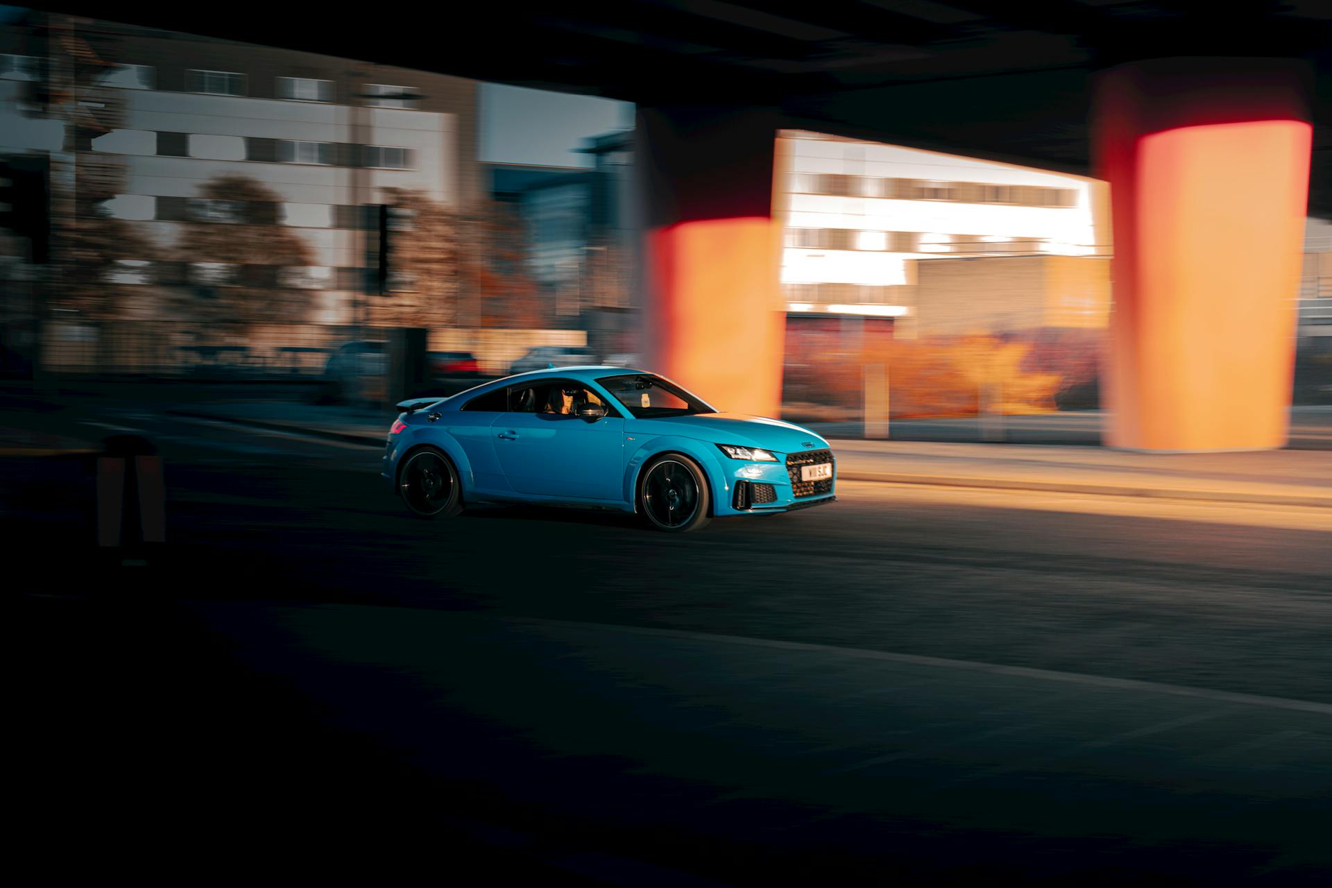 A vibrant blue car speeds through an urban Scottish cityscape at dusk, emphasizing motion and architectural elements.