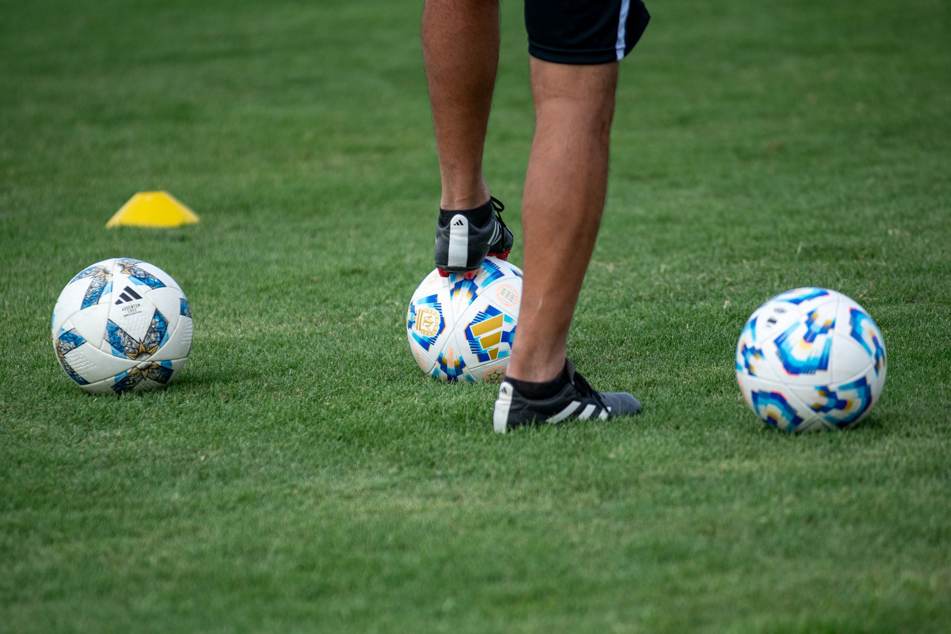 A coach inspecting a beginner’s cleat studs beside a wet football field before evening practice