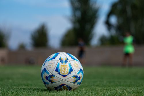 Free Soccer ball on a grassy field with blurred players in the background, outdoors. Stock Photo