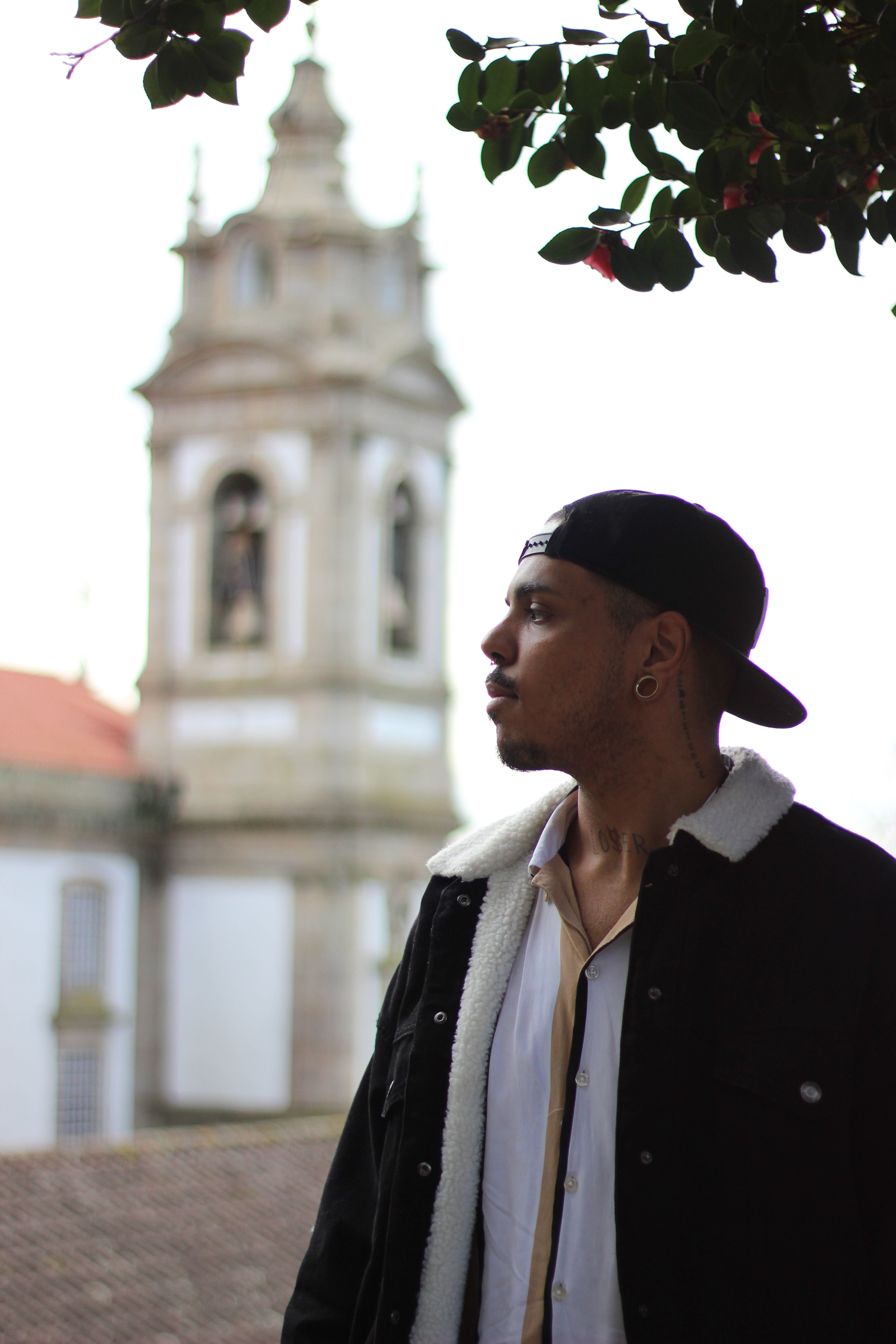Man in Braga, Portugal, with a historic tower backdrop, showcasing urban style.