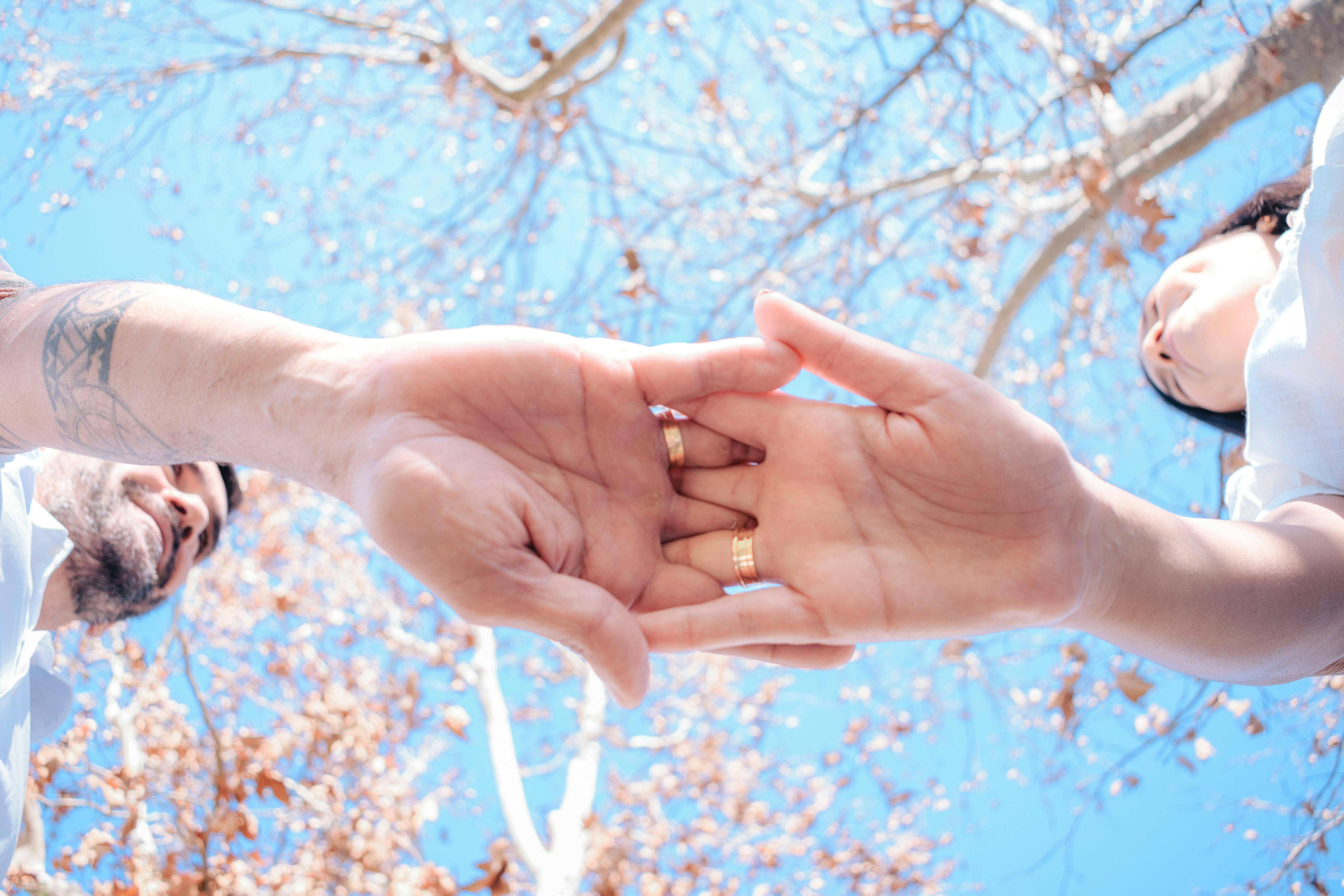 Free A tender moment between a couple holding hands under a bright blue sky with autumn leaves. Stock Photo