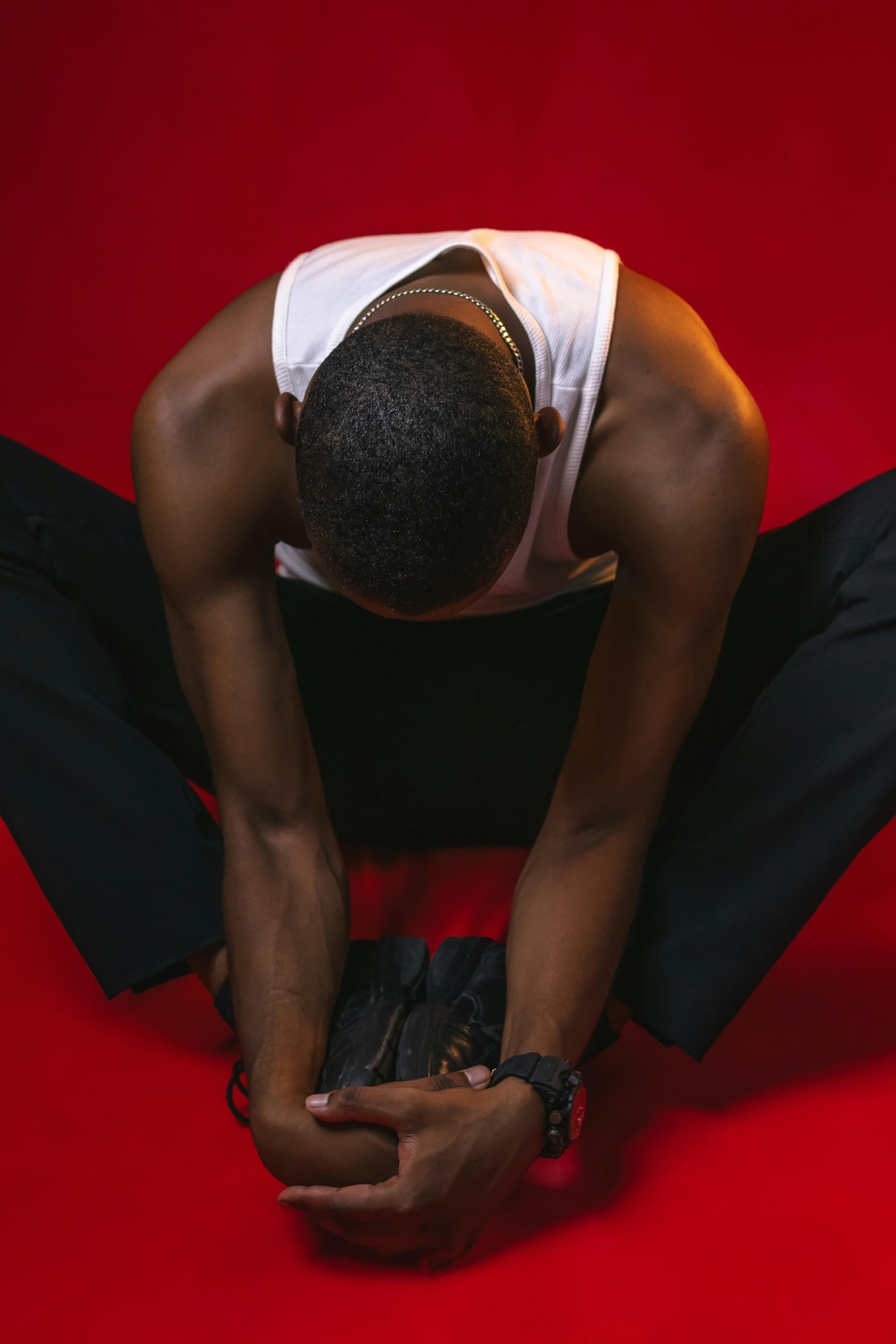 Young man seated on red background, leaning forward in a reflective pose.