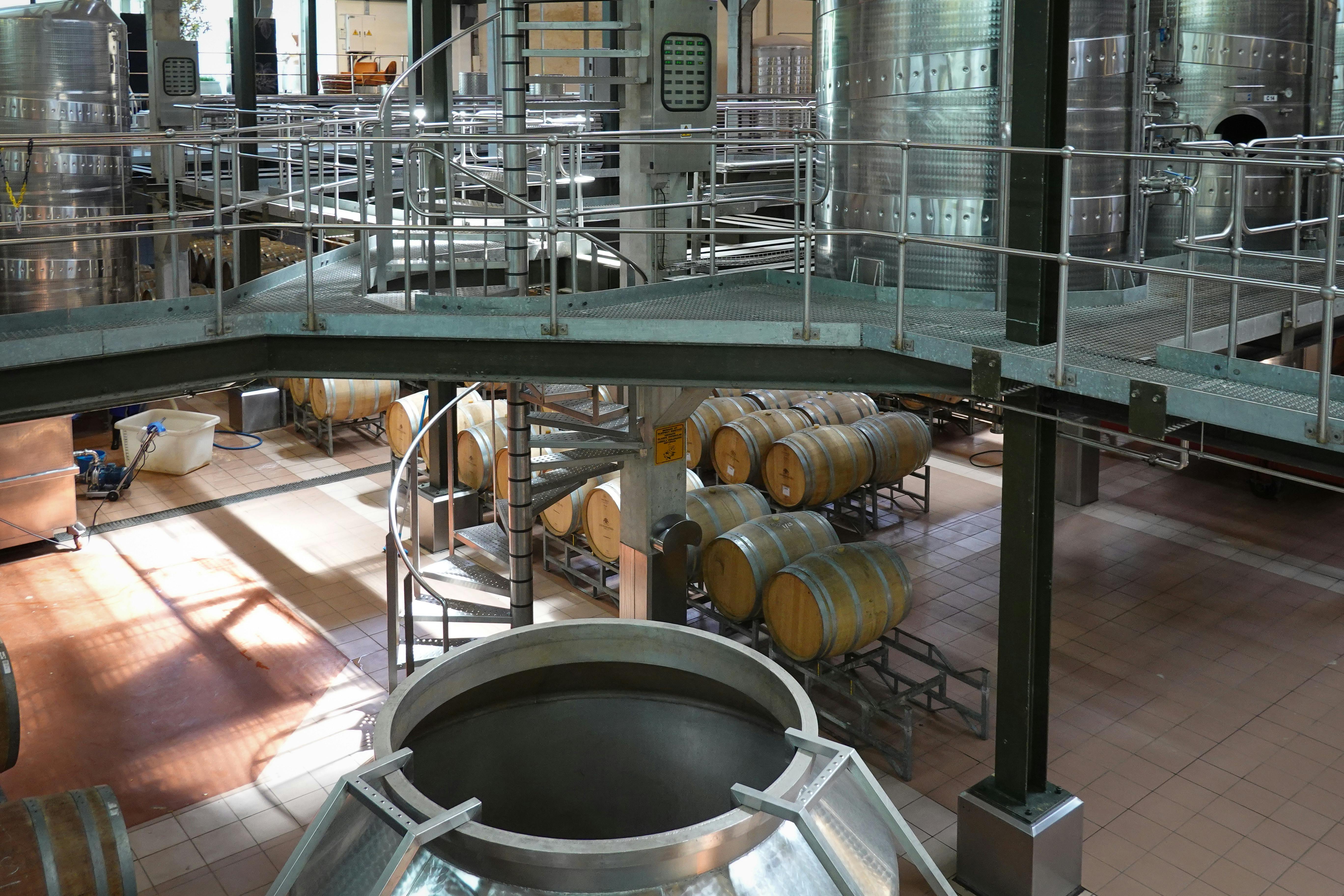 Interior view of a modern wine cellar featuring wooden barrels and large steel fermentation tanks.
